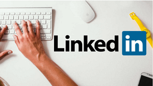 a color, real life picture of an arm and hand of a white man typing on a key board and LinkedIn