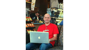 A picture of Anthony Trustee sitting in a coffee shop in his computer